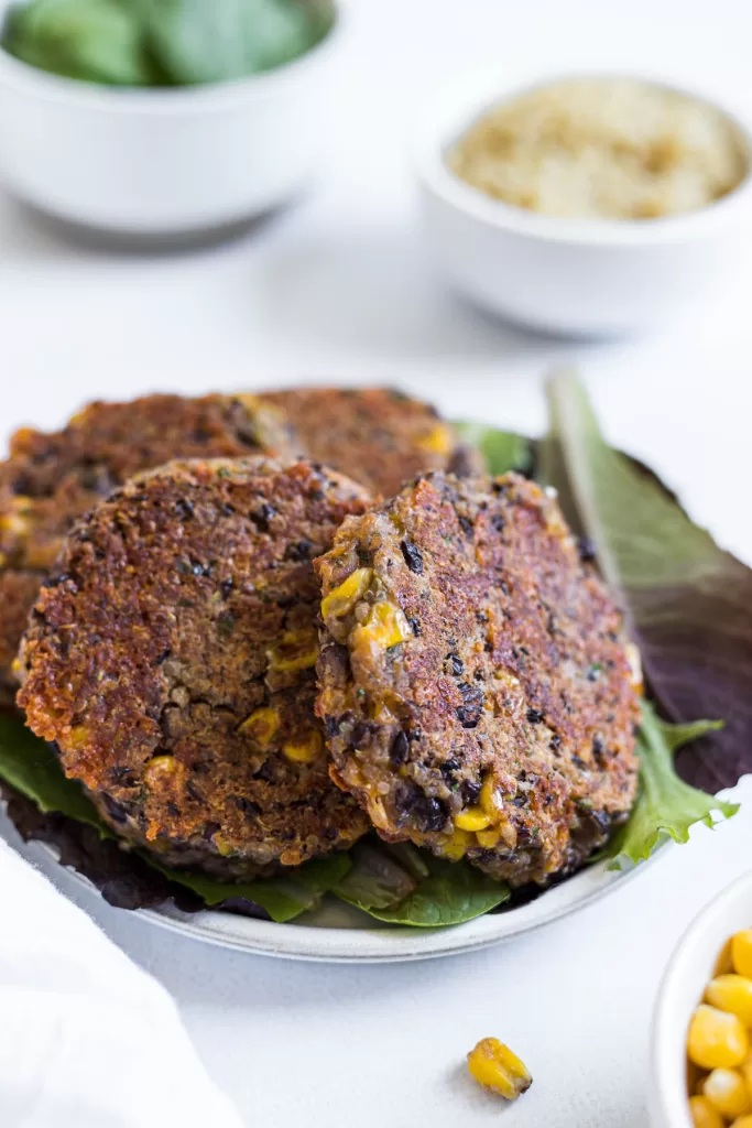 Black bean fritters are stacked next to each other over a bed of lettuce.