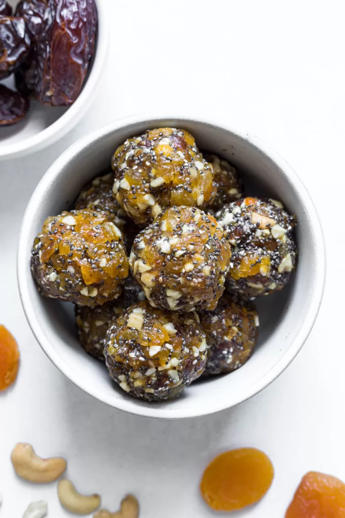 An overhead view of apricot energy balls in a bowl with apricots, cashews, and dates surrounding it.