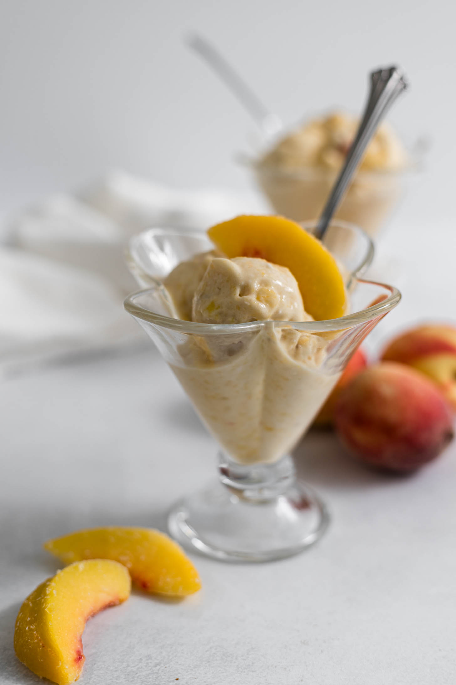Peach nice cream in an ice cream glass with a peach on top.