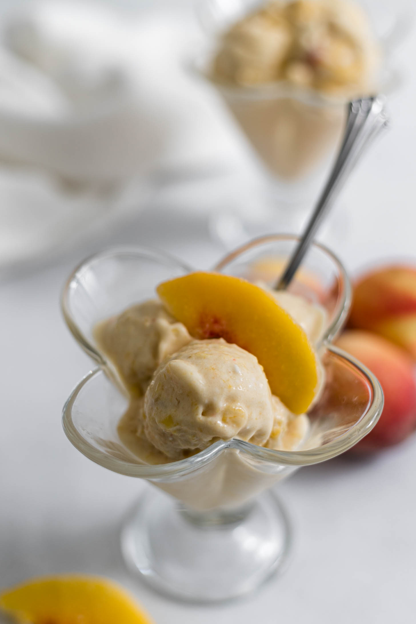 Close up of a scoop of peach nice cream with a peach slice on top of it.