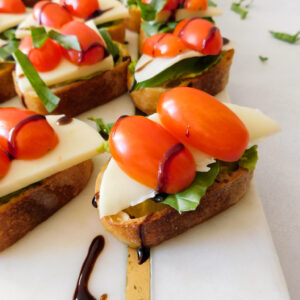A close up of Avocado Caprese Crostini with more crostini in the background. They're sitting on a white marble serving board.