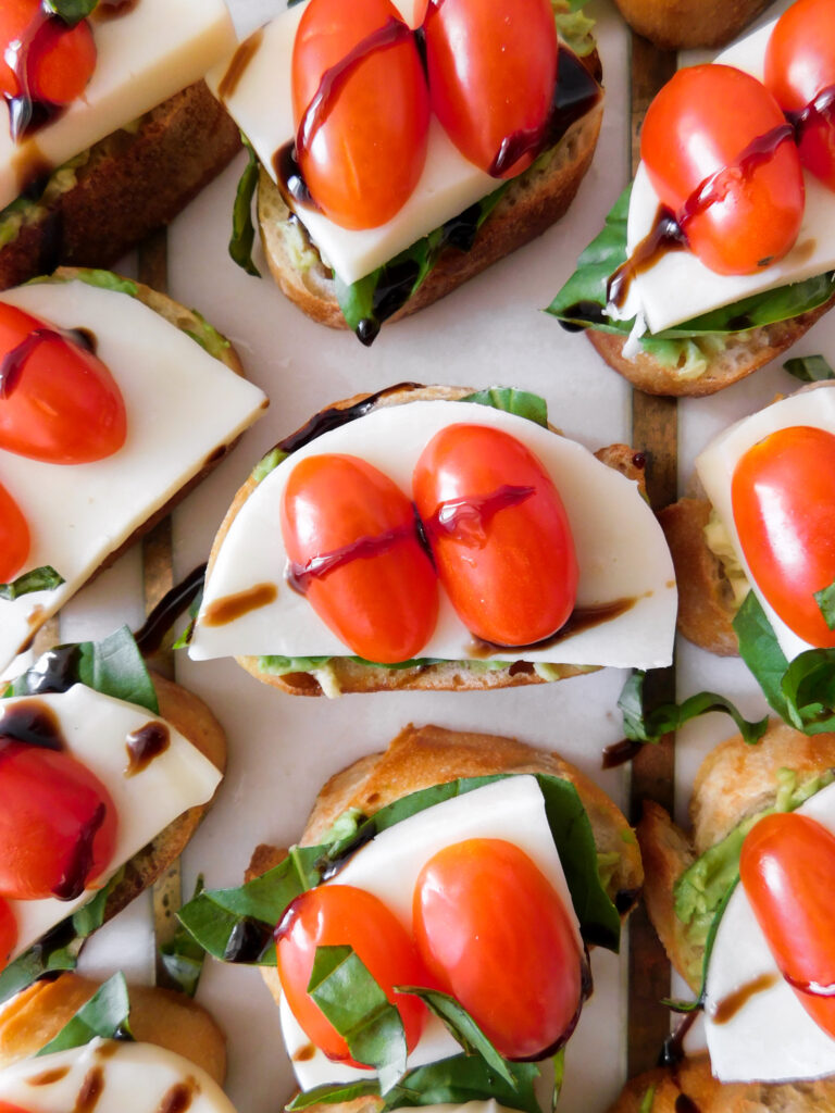 A close up view of an Avocado Caprese Crostini with more crostini surrounding it.