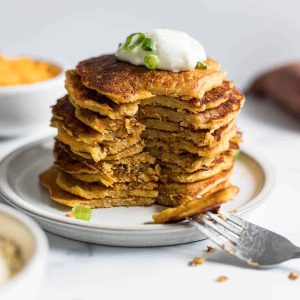 A stack of Savory Sweet Potato Pancakes with a section cut out with a fork.