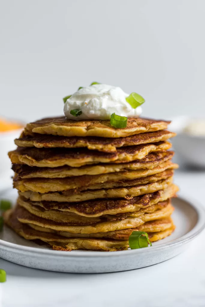A stack of pancakes with plain yogurt on top and green onions.