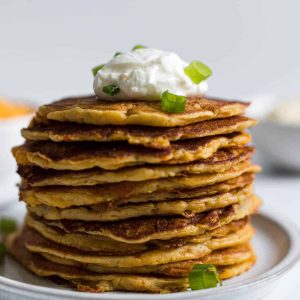 A stack of pancakes with plain yogurt on top and green onions.