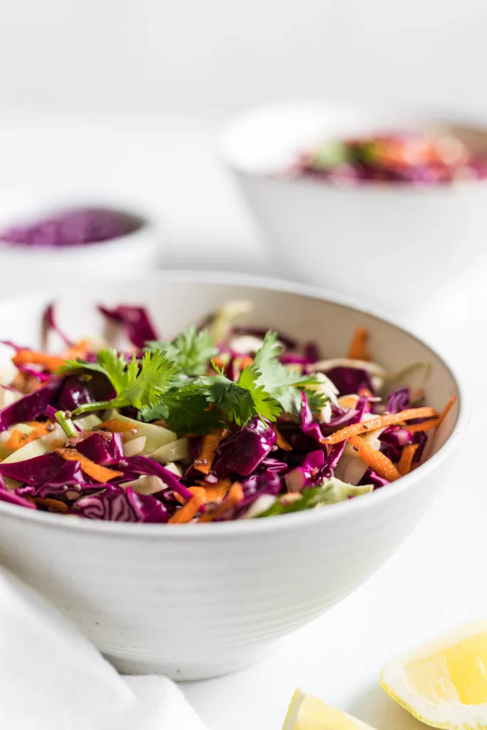 A side view of coleslaw in a white bowl. Another bowl sits in the background with coleslaw.