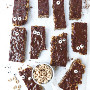 Monster bars are spread out on parchment paper with a cup of cheerios in the middle of the image.