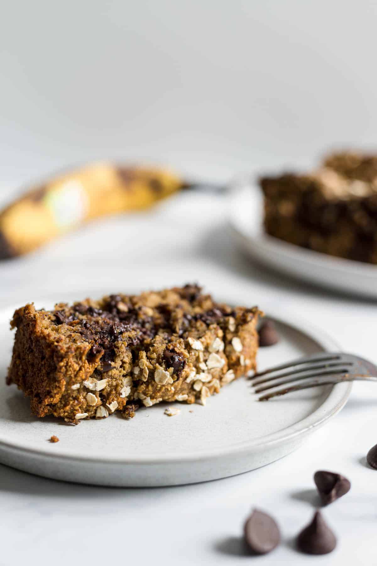 A single slice of banana chocolate chip bread on a plate with a fork resting on it.