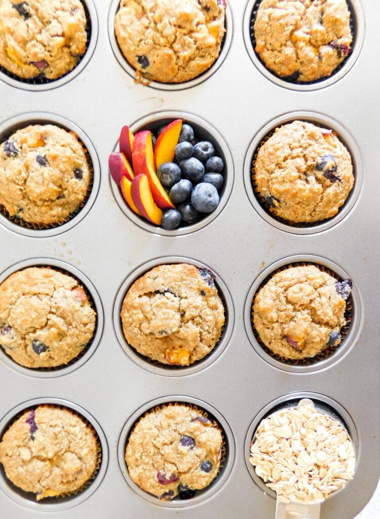 Muffins in a muffin tin, one of the holes is filled with blueberries and nectarines instead of a muffin.