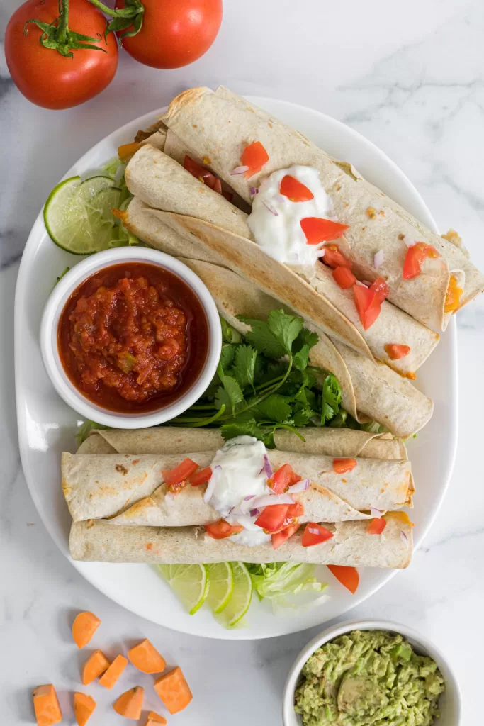 A plate of flautas with a small bowl of salsa.