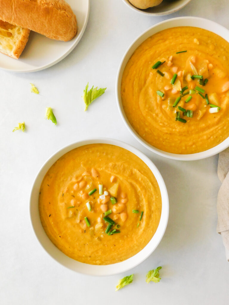 Two bowls of White Bean Potato Soup and a plate with a baguette on it.