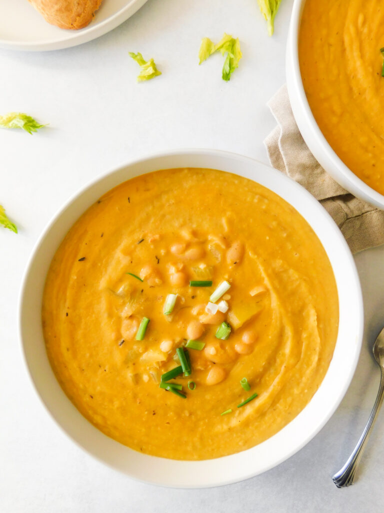 A bowl of Creamy Vegan White Bean Potato Soup with a spoon next to it. Another soup bowl sits on a linen cloth next to it. 