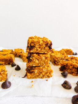 A stack of three healthy pumpkin bars. Around it are several more pumpkin bars with chocolate chips scattered next to them.