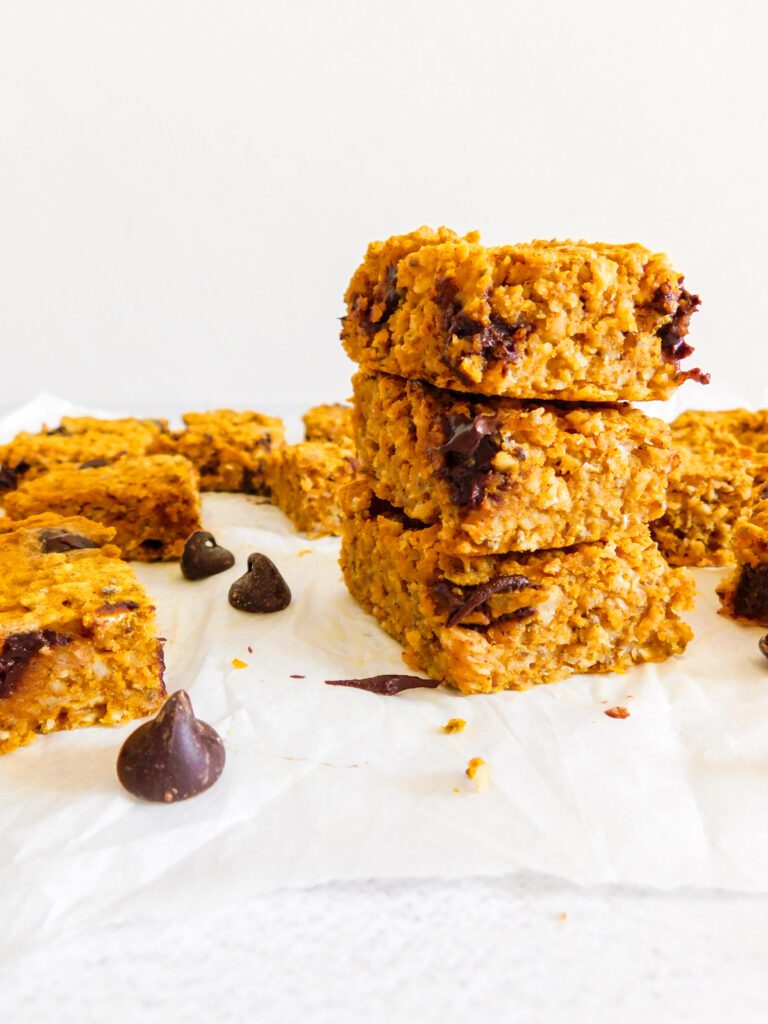 There is a stack of healthy pumpkin bars with other bars arranged around the stack along with several chocolate chips.