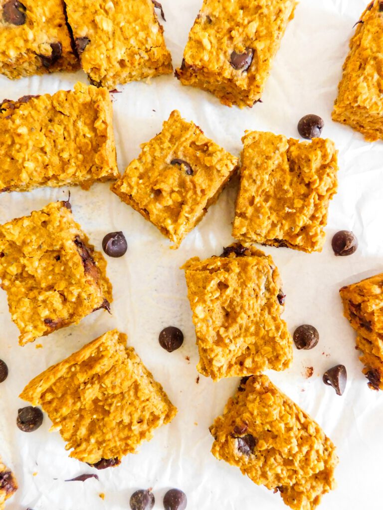 Healthy Pumpkin Bars lay scattered on parchment paper in an overhead view with chocolate chips arranged in between the bars.