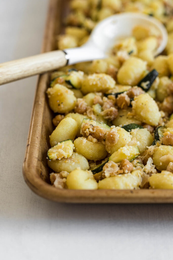 A tray of sheet pan gnocchi with a serving spoon in it.
