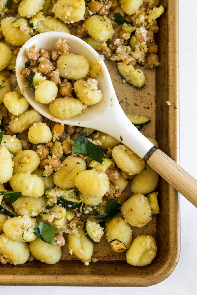 A sheet pan of gnocchi with a serving spoon in it that has a scoop of gnocchi in it.