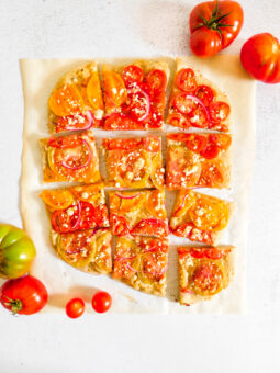 An overhead view of Hummus Pizza cut into slices with tomatoes next to it.
