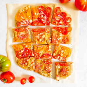 An overhead view of Hummus Pizza cut into slices with tomatoes next to it.