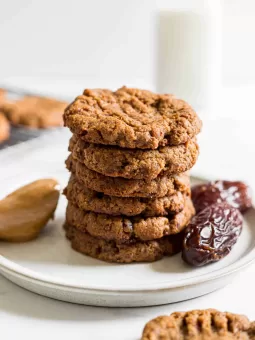 A stack of peanut butter date cookies with dates and peanut butter next to it and a glass of milk behind it.