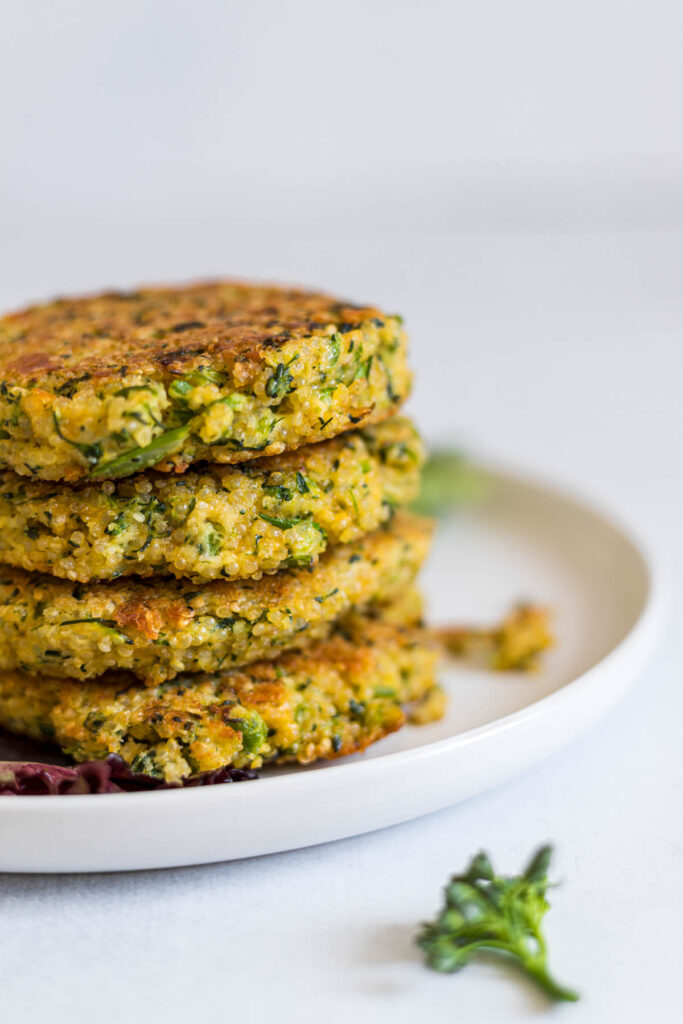 A stack of Cheesy Broccoli Quinoa Patties on a plate. A piece of broccoli lays to the side.