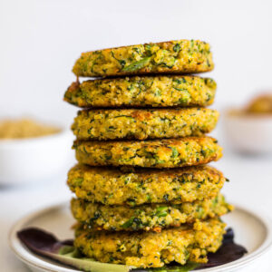 A tall stack of quinoa patties sit on a plate. A few pieces of broccoli sit in front of it.