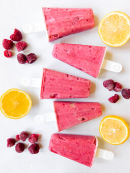 A row of raspberry popsicles with raspberries and lemons next to it.