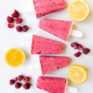 A row of raspberry popsicles with raspberries and lemons next to it.