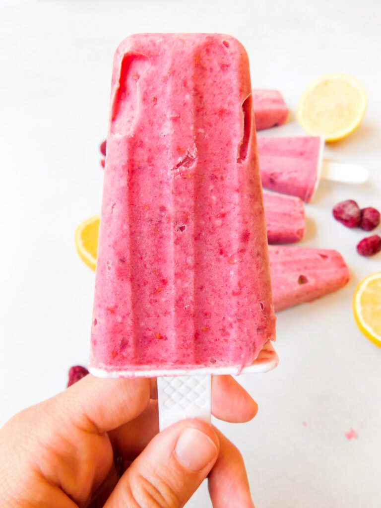 A white hand is holding up a raspberry lemonade popsicles.