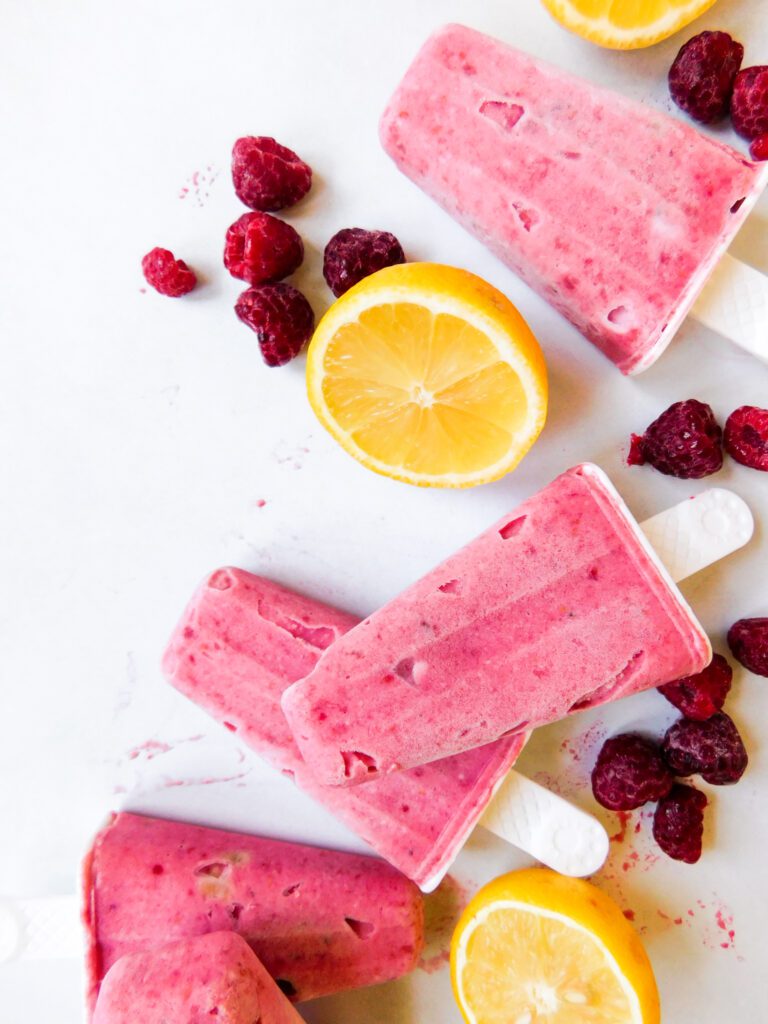 Raspberry Lemonade Popsicles spread out with raspberries and lemons next to it.