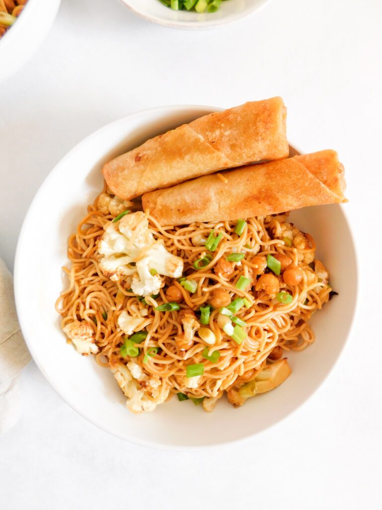 A bowl of ramen noodles with two spring rolls in the bowl as well.