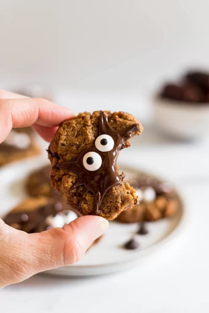 A white hand is holding up a cookie with a bite taken out of it.