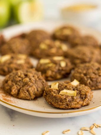 A plate of apple peanut butter cookies with green apples in the background.