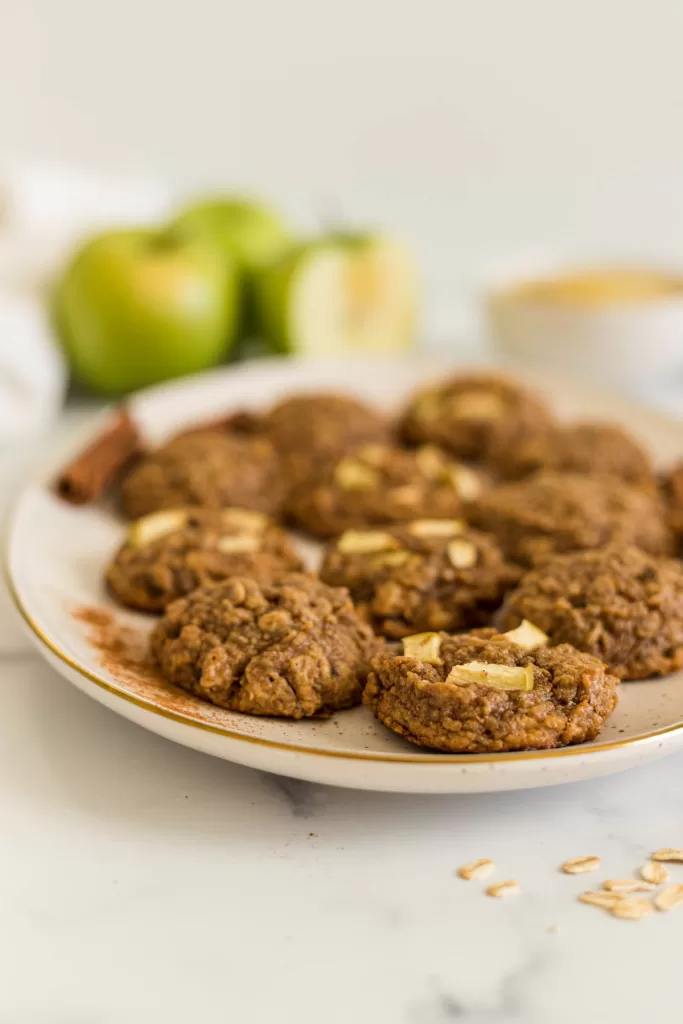 A plate of apple cookies with green apples behind it.
