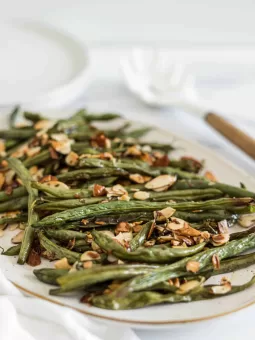 A side view of a plate with crispy roasted green beans with slivered almonds.