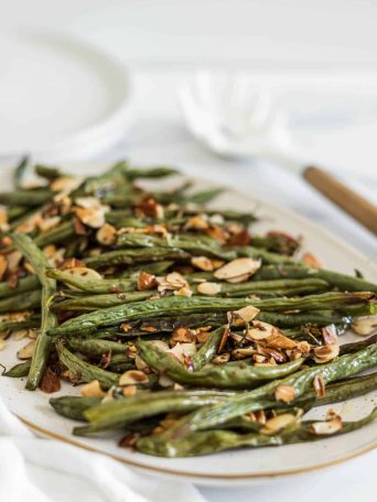 A side view of a plate with crispy roasted green beans with slivered almonds.