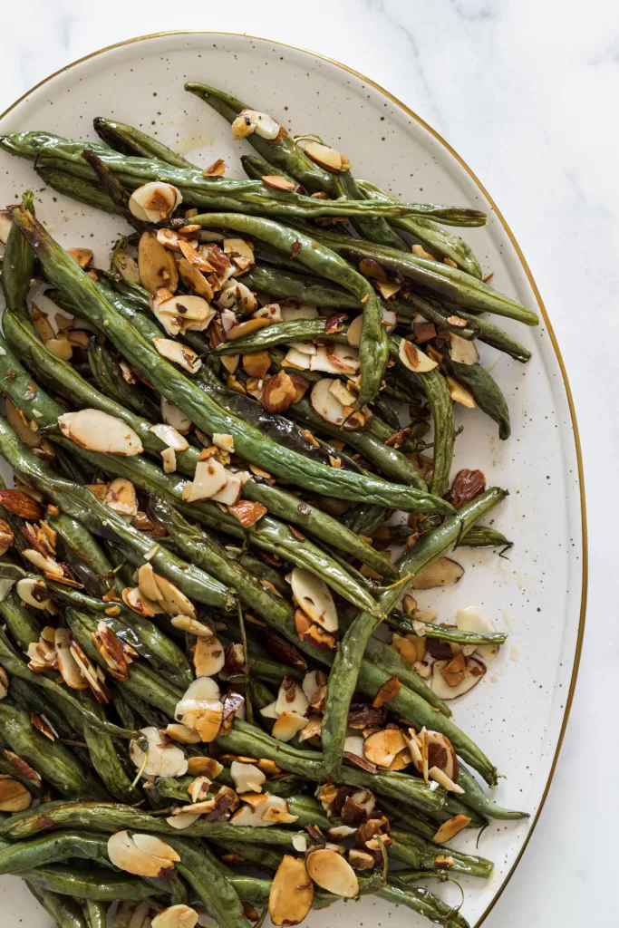 A close overhead view of roasted green beans on a plate with toasted almonds. 