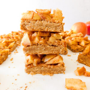 A stack of Easy Apple Pie Bars with more bars surrounding it and two apples in the background.
