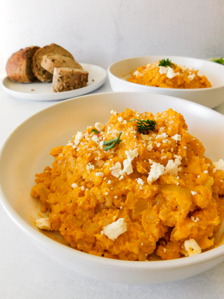 A side view of two bowls of roasted butternut squash risotto with a plate of bread off to the side.