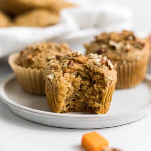 Sweet potato zucchini muffins on a plate, one with a bite out of it.