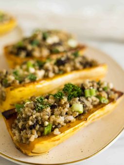 Side view of three vegetarian stuffed delicata squash boats on a plate.