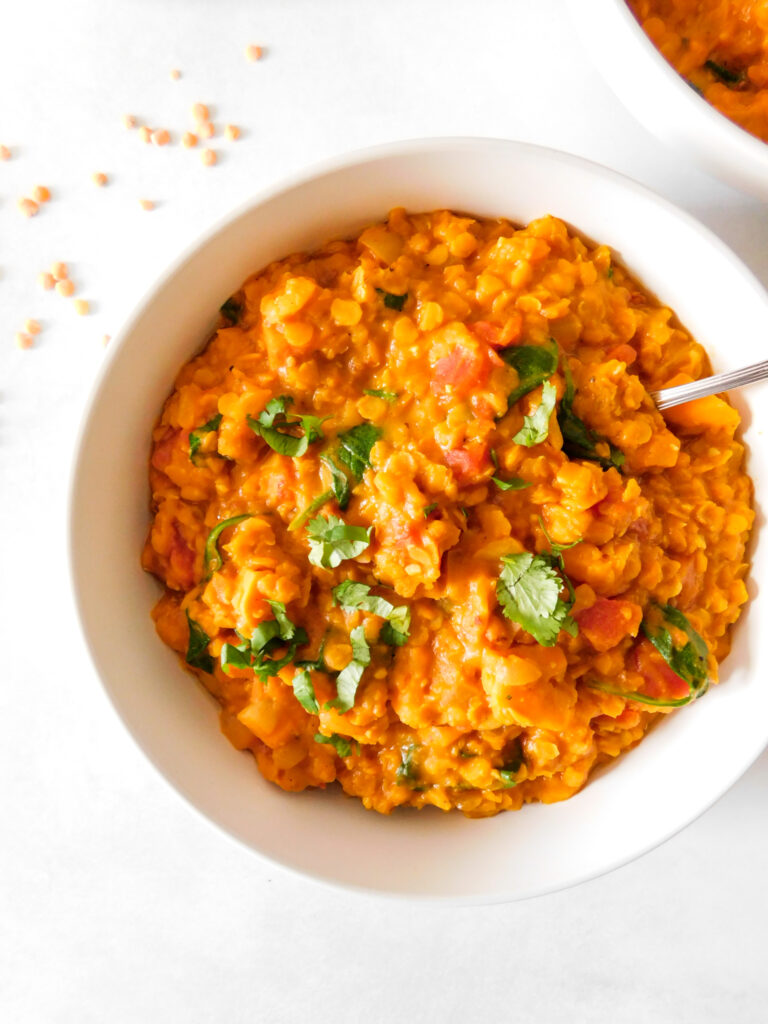 A bowl of red lentil curry with some dried red lentils sprinkled next to it.