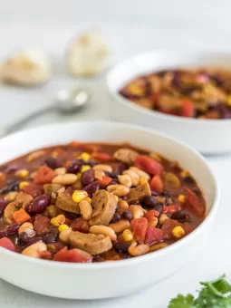A side view of a bowl of Easy 25-Minute Vegan Chili with another bowl in the background, along with a spoon and some bread chunks.