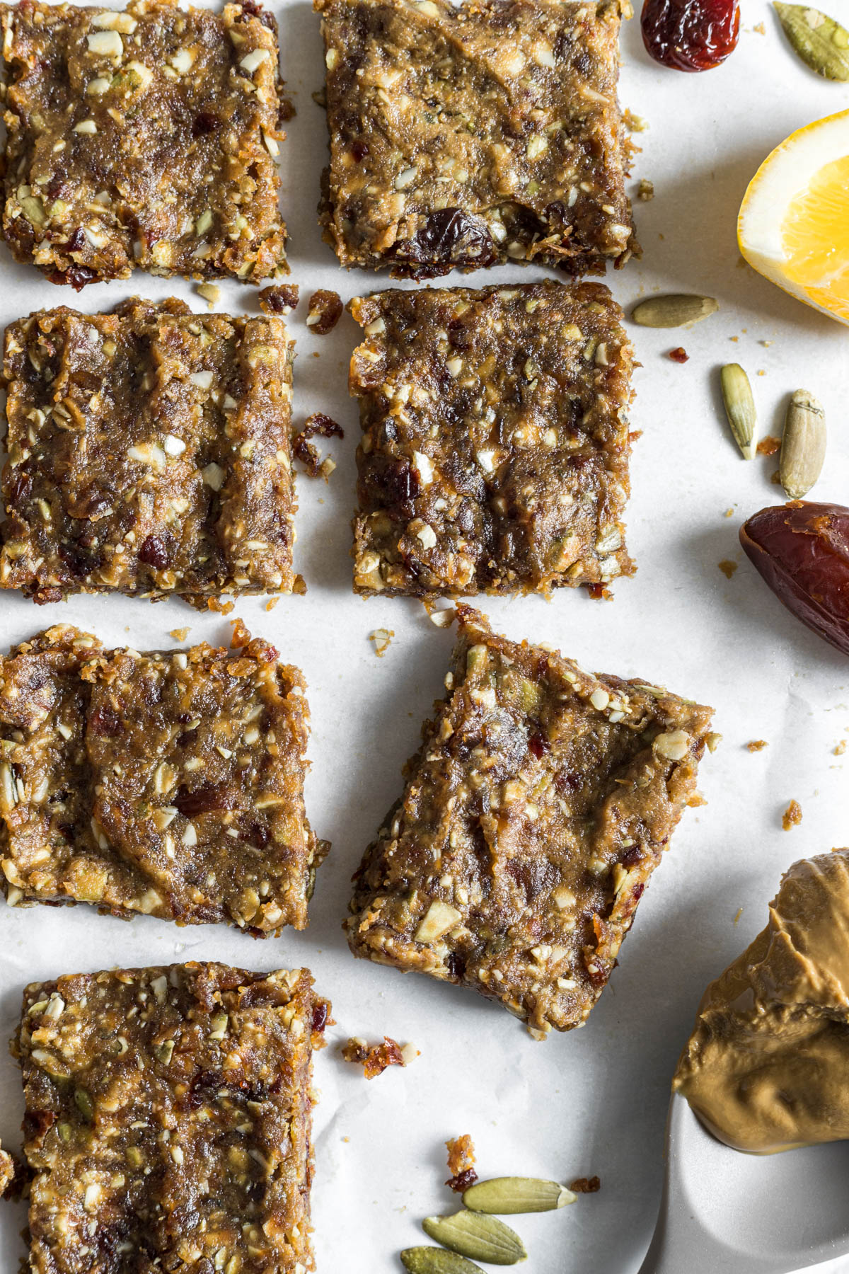 Nut-Free Protein Bars are lying in rows, with one slightly turned. Some sunflower butter, pumpkin seeds, and lemon sit next to the bars.