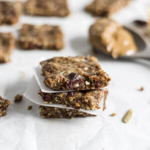 A stack of three Nut-Free Protein Bars. More bars sit in the background as well as a spoon with sunflower butter on it.