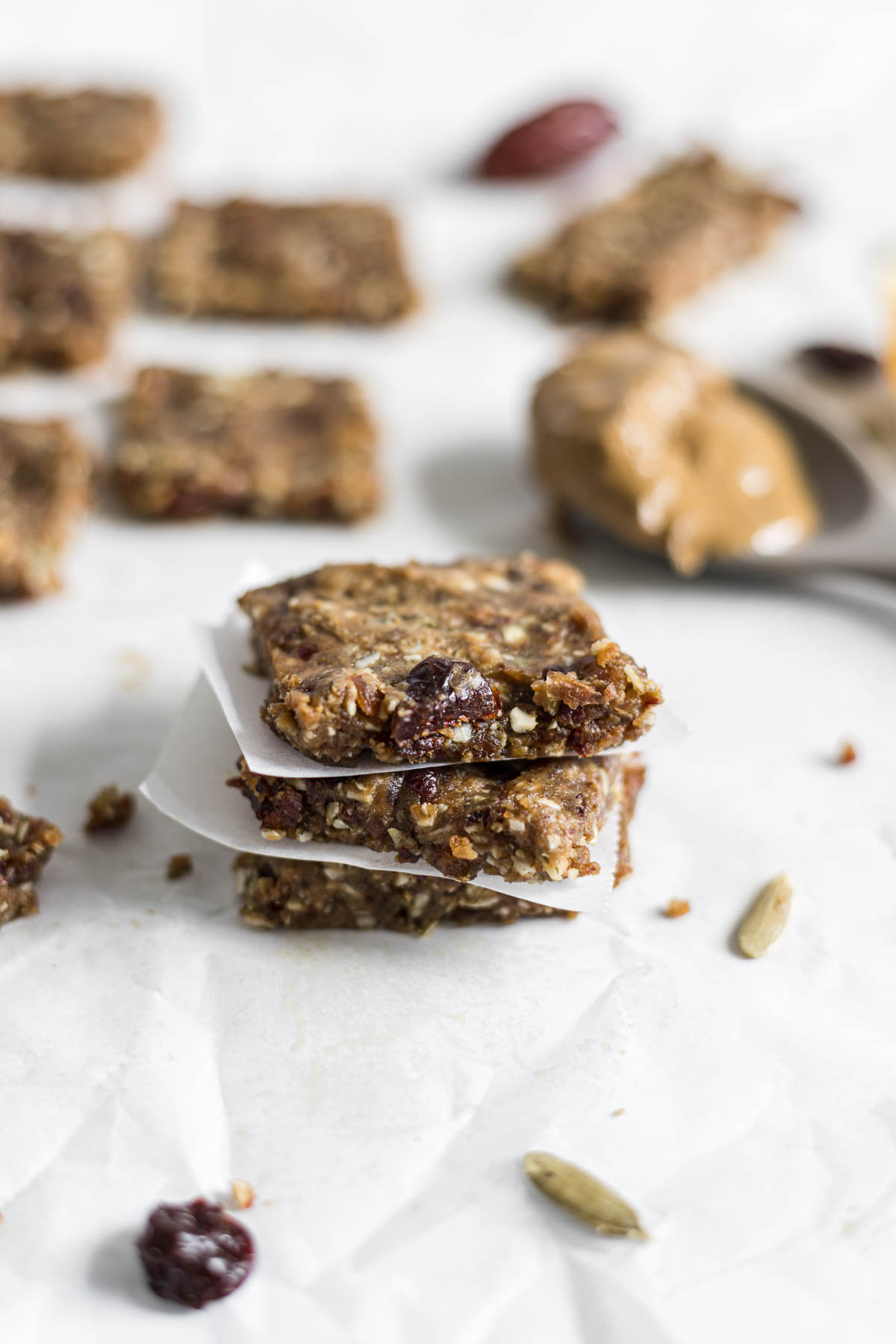 A stack of three Nut-Free Protein Bars. More bars sit in the background as well as a spoon with sunflower butter on it.