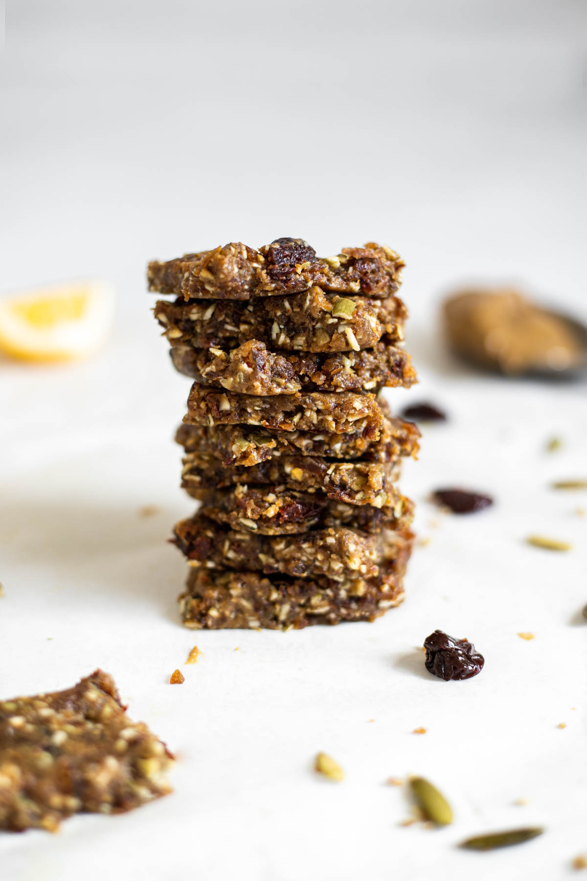 A tall stack of protein bars. A lemon wedge and spoon with sunflower butter sit in the background.