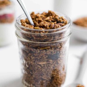 A jar of steel-cut oats granola with a spoon in it. A spoonful of granola sits next to it.