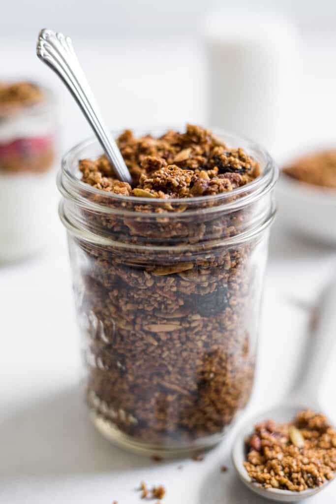 A jar of steel-cut oats granola with a spoon in it. A spoonful of granola sits next to it.