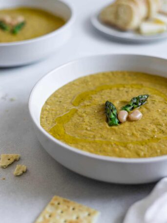 A bowl of Asparagus Broccoli Soup with bread in the background.